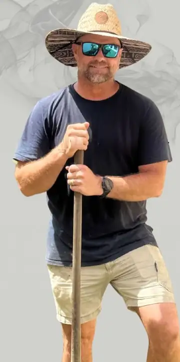 Mick Woodward in a straw hat and sunglasses, leaning on a shovel